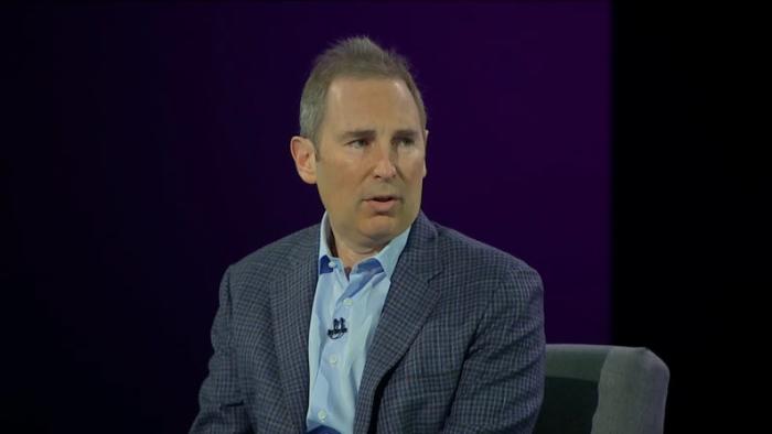 Amazon CEO Andy Jassy, sitting with a strange look on his face in an interview with a black backdrop behind him.