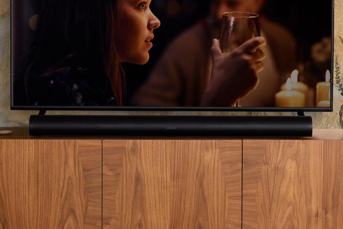 The Sonos Arc sits on a wooden cabinet with a TV above it. 