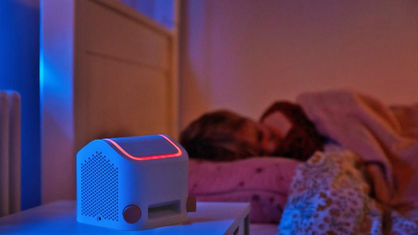 The Yoto Player (third-generation) sits on a bedside table next to a sleeping child at night. 