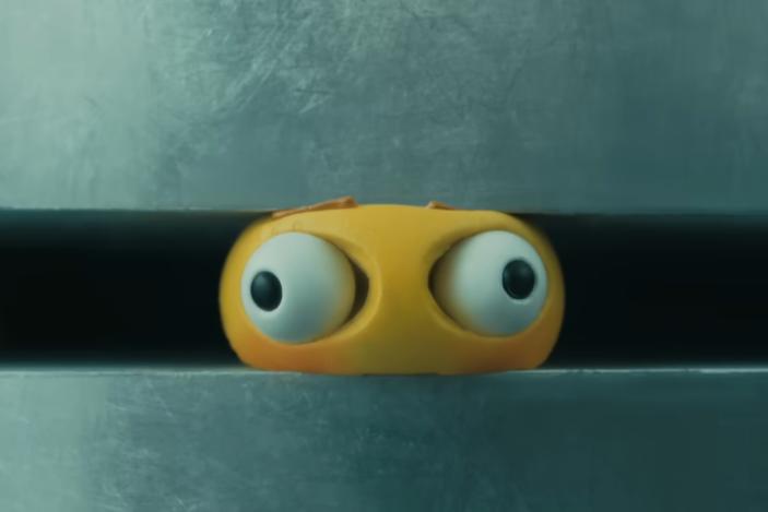 A yellow emoji being crushed in an industrial crusher. Its eyes bulge out of its head.