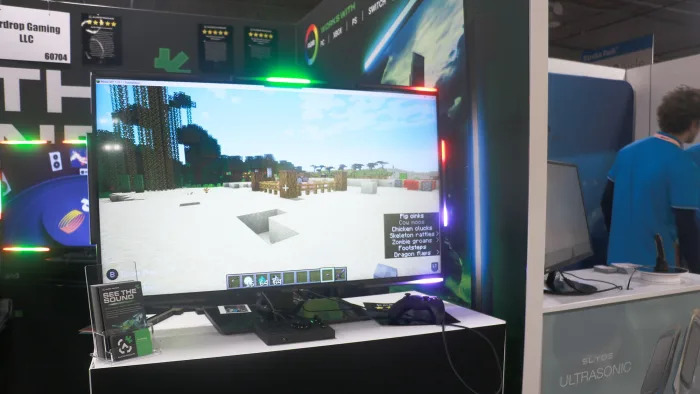 A monitor on a table, with the screen showing an environment in Minecraft. Surrounding the display are lights, with the middle top bar glowing in green, while those in the top right corner are showing red. The bottom corner is lit up in purple.