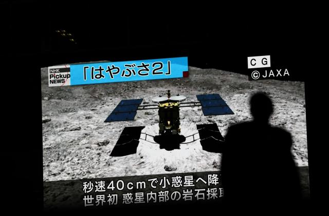 In this picture taken on July 10, 2019 a man walks past a screen displaying a computer-generated image of the Hayabusa2 probe, during a news broadcast at Akihabara district in Tokyo. - Japan's Hayabusa2 probe landed successfully on a distant asteroid for a final touchdown on July 11, 2019, hoping to collect samples that could shed light on the evolution of the solar system. (Photo by Behrouz MEHRI / AFP)        (Photo credit should read BEHROUZ MEHRI/AFP/Getty Images)