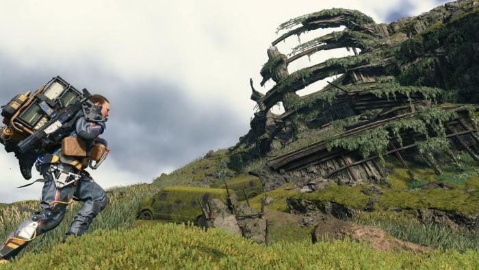 A male character bearing an overladen backpack climbs a grassy hill. A decaying circular structure is in the background.