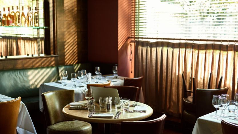 Empty restaurant prepared for evening meal with computer on table and place settings