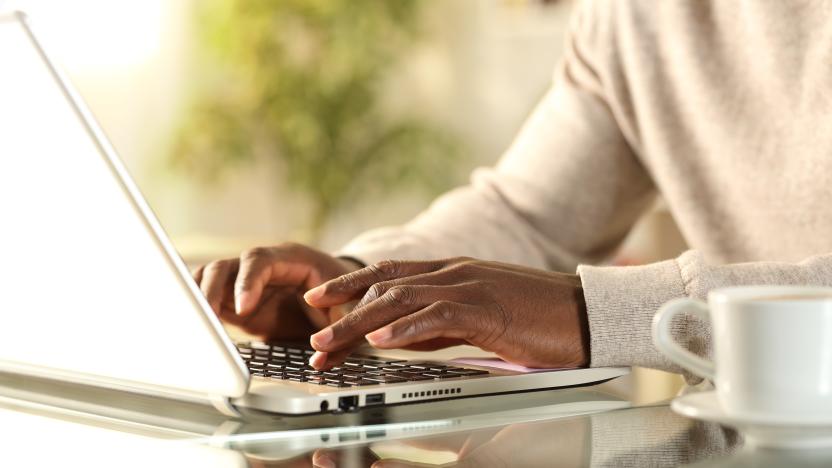 Close up of black man hands typing on a laptop sitting on a desk at home