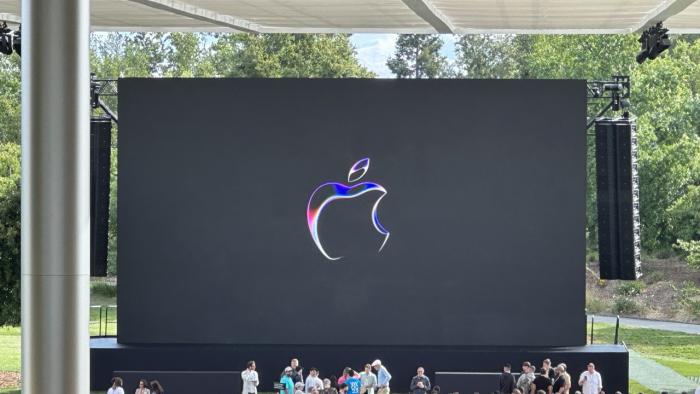 The Apple logo on a black screen with a stage and rows of seats in front of it.