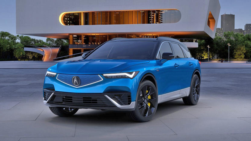 Marketing photo of the Acura ZDX electric SUV. The vehicle, in blue trim, sits in front of a modern building.