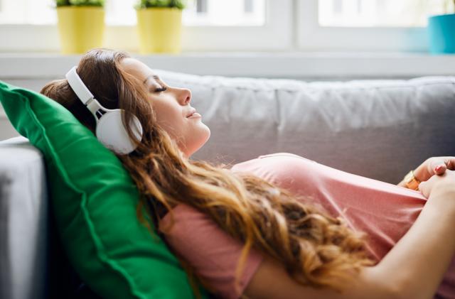 Portrait of a beautiful young woman lying on sofa with headphones on and closed eyes, relaxing