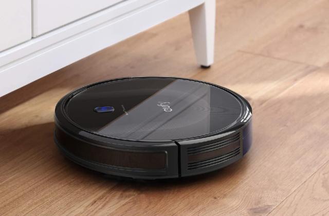 the eufy BoostIQ RoboVac 11S MAX robot vacuum is running on a hardwood floor and about to clean under a cabinet. 