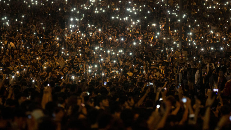 Nighttime shot of countless protestors holding up their phones’ flashlights.