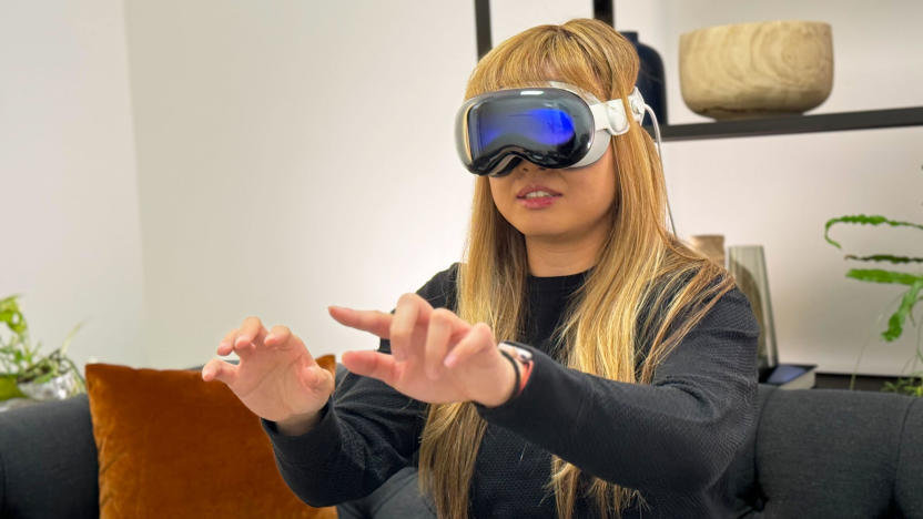 A woman with blonde hair with the Apple Vision Pro on her face, her hands are outstretched with her fingers held in a typing position.