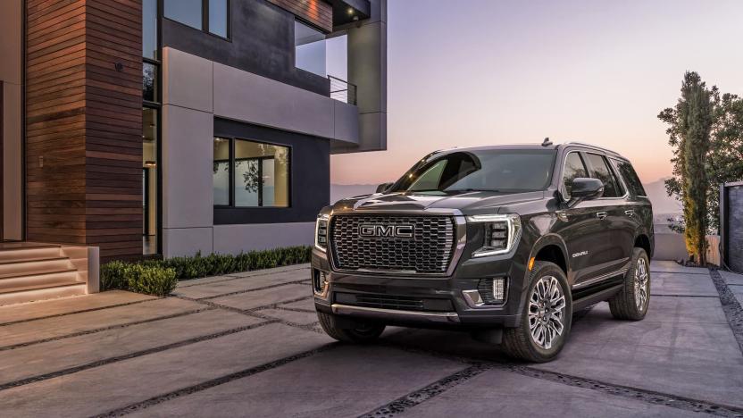 A 2023 GMC Yukon Denali Ultimate is parked out front of a fancy modern home at dusk.