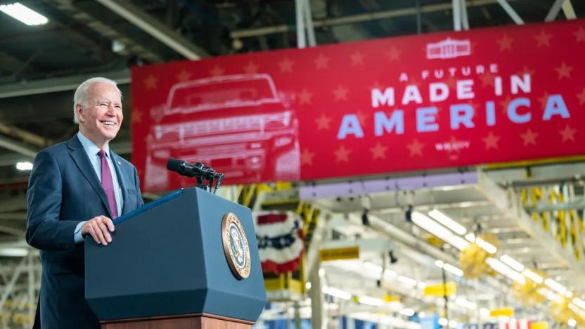 President Joe Biden standing at a podium in an auto factory. A sign behind says "A Future Made in America."