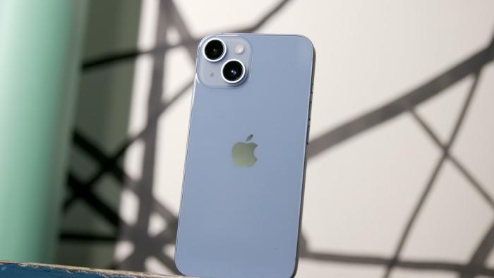 The blue iPhone 14 standing on a shelf with its dual rear cameras facing out.