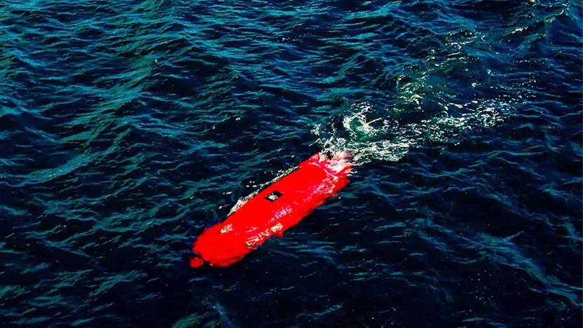 The Dive Technologies autonomous underwater vehicle seen in red as it moves across the water just below the surface of the ripples.