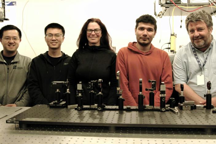 Group photo of five members of a research team focused on a scientific camera. They stand smiling in a laboratory with various imagine equipment on the research table in front of them.