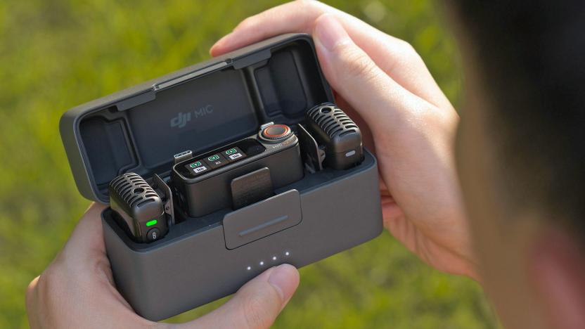 An over-the-shoulder view of DJI's updated Mic 2 in its charging case being opened by someone with blurred grass in the background.