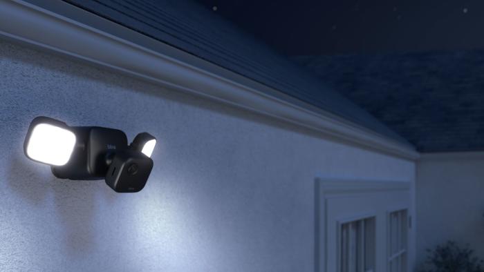 Image of the Blink Outdoor 4 with its external floodlight mount, sold separately, projecting light into the darkness. 