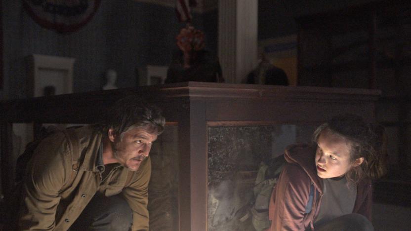 A still from 'The Last of Us' TV show, showing two people crouching down behind a table.