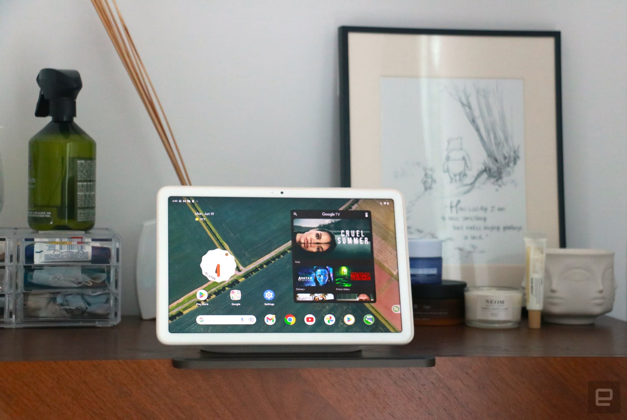 The Pixel Tablet on its dock on a walnut chest of drawers showing the Android home screen. 