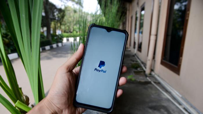 A man seen hold a smartphone with the logo PayPal in Bogor, West Java, Indonesia on July 30, 2022. The Indonesian Ministry of Communication and Information has blocked several applications related to the registration of Electronic System Operators (PSE) as an effort by the Indonesian government to protect public consumers, including PayPal Inc platform. (Photo by Adriana Adie/NurPhoto via Getty Images)