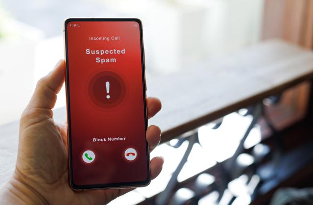 A man receiving an incoming suspected spam call on her phone. The network provider detect the scam and show warning sign to rejects the call.