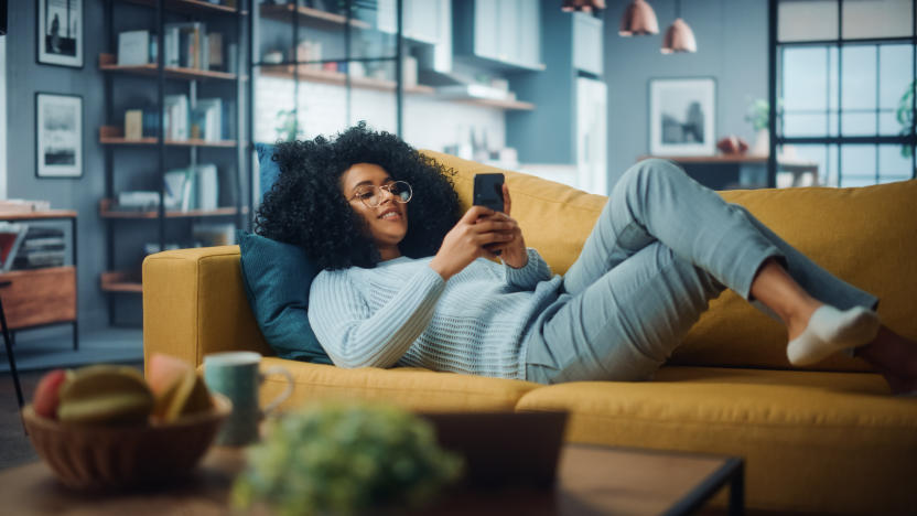 Happy Beautiful Latina Female Using Smartphone in Cozy Living Room at Home. Female Resting on Comfortable Sofa. She's Browsing the Internet and Checking Videos on Social Networks and Having Fun.