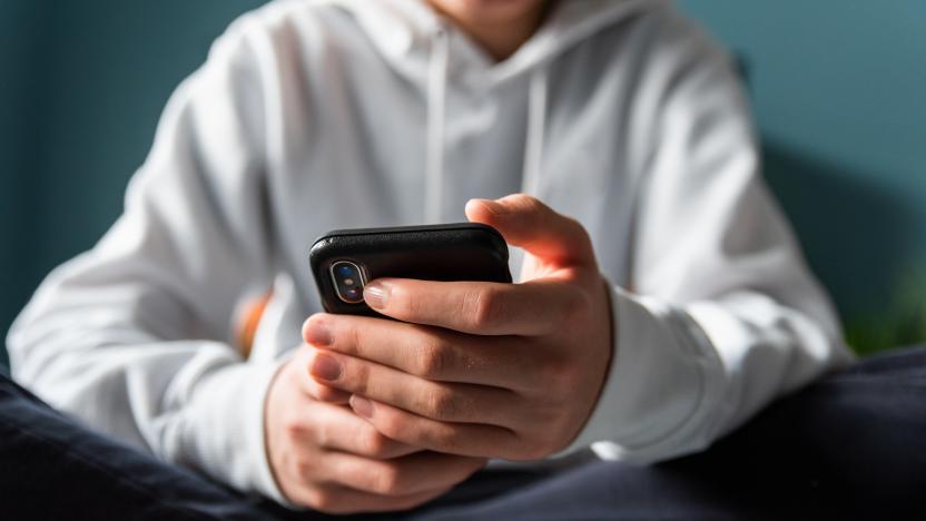 Close up of hands of teen boy in white sweater texting on phone.