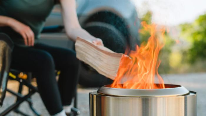 A cropped image showing someone in a camping chair feeding wood into the Ranger fire pit by Solo Stove.