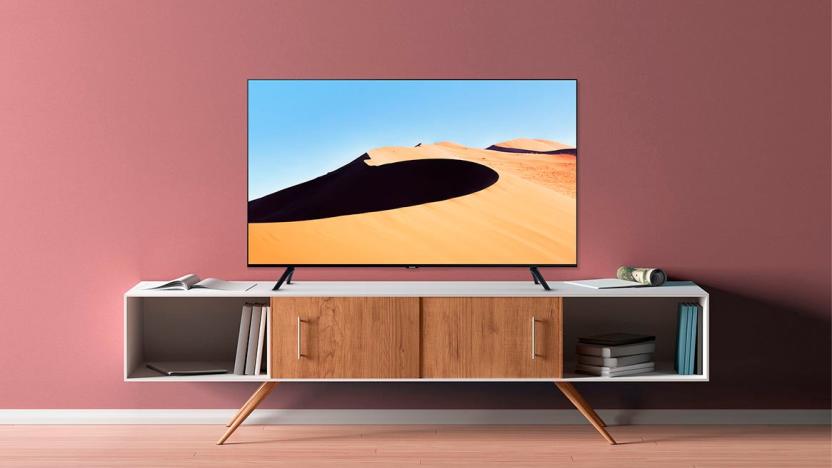 A press image of the Samsung TU690T 4K TV, displaying a TV on a white and brown cabinet against a light red wall. The image on the TV displays a desert dune.