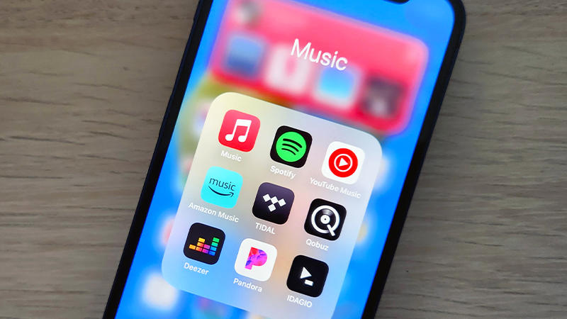 A smartphone lies on a desk, displaying icons for several music streaming apps.