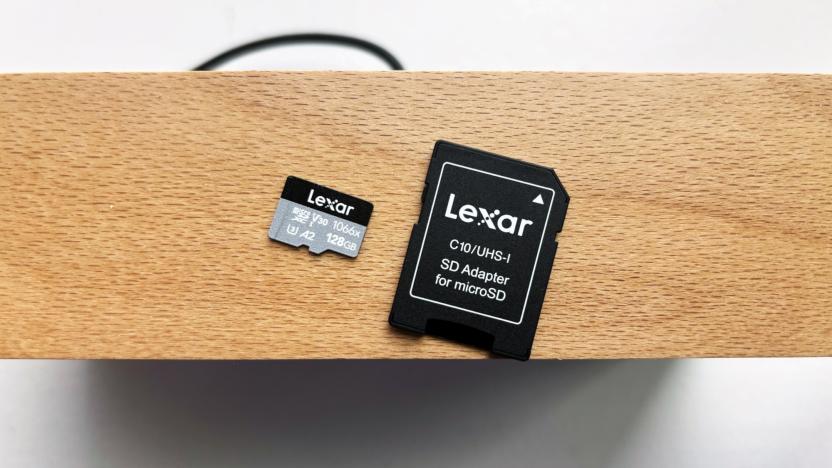 A silver and black Lexar Professional 1066x microSD card and its black SD card adapter rest on top of a brown wooden shelf above a white window sill.