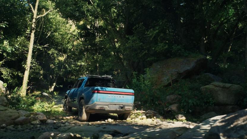 A blue Rivian R1T EV in a tropical river creek. 