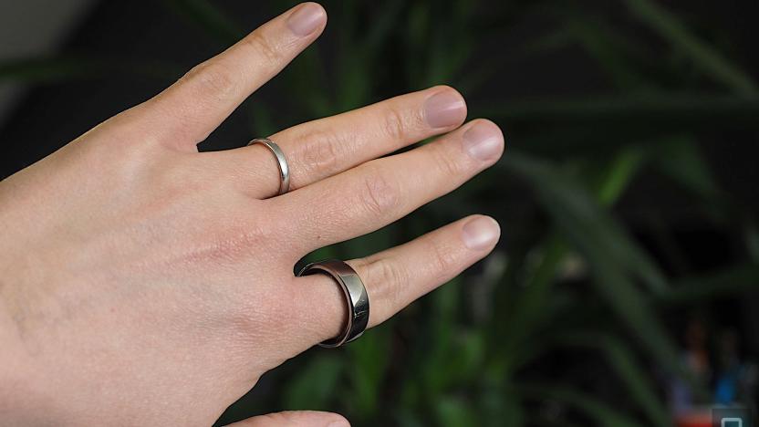 Image of a hand wearing an Oura Ring on the index finder in front of a dark green plant.