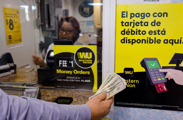 A person holds cash in his hand next to Western Union signs at a Florida Check Cashing window inside a convenience store in Miami, Florida, on January 12, 2023. - Western Union announced January 11, 2023 it had resumed moving money from the United States to Cuba, more than two years after sanctions forced the US-based firm to shut down operations on the communist-run island. The resumption of money transfer services to Cuba "is currently in a test phase," the company said in a statement, noting that US customers are limited to sending a maximum of $2,000 per day and only from select sites in the Miami area. (Photo by Eva Marie UZCATEGUI / AFP) (Photo by EVA MARIE UZCATEGUI/AFP via Getty Images)