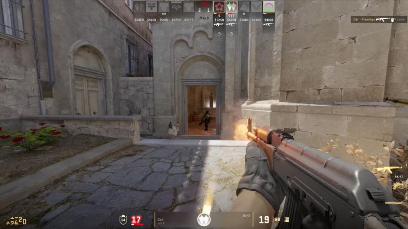 Screenshot from Counter-Strike 2, showing a player (first-person perspective) holding an automatic rifle, firing towards a soldier in the distance. Outdoor environment featuring an older cathedral-style building.