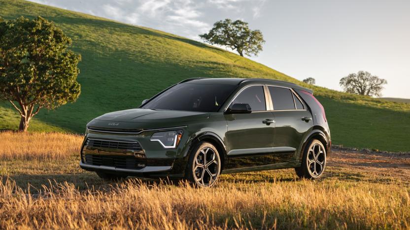 A dark green Kia Niro 2023 parked in a field next to a green grassy hill.