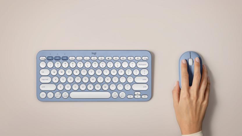 A blue Logitech Pebble 2 keyboard and mouse seen from above on a blank table top with a hand grasping the mouse.