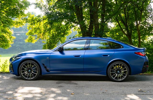 A blue BMW i4 M parked on a bucolic roadside near a lake.