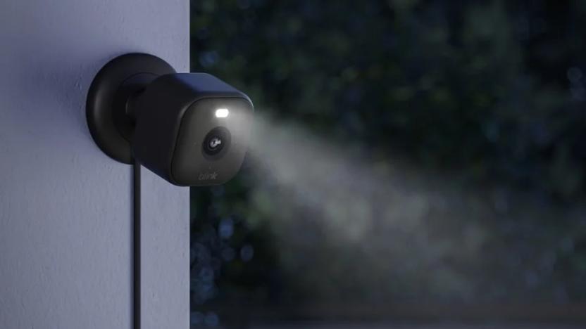 The new Blink Mini 2 camera in black shown mounted to an outside wall at nighttime with the LED spotlight shining