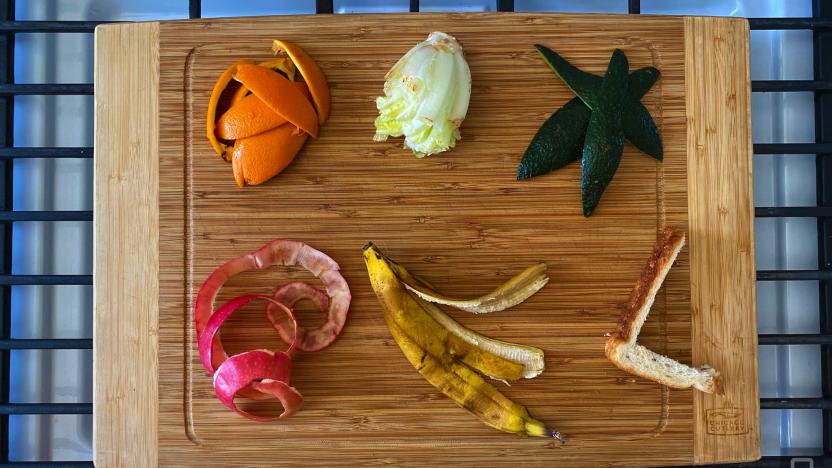 Food scraps, including lettuce, sandwich crust and peels from an orange, apple and banana, are arranged on a bamboo cutting board. 