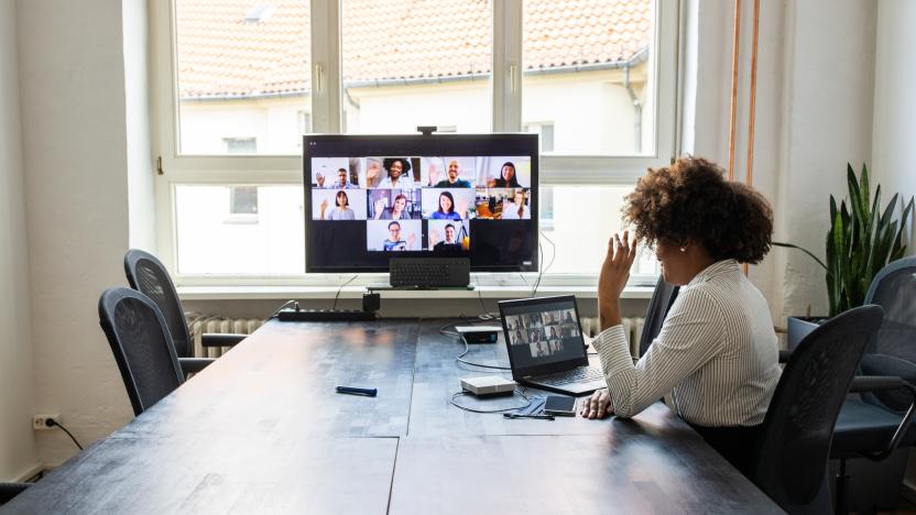 Rear view of a businesswoman having a meeting with team over a video conference in office board room. Meeting over a video call in office post pandemic lockdown.