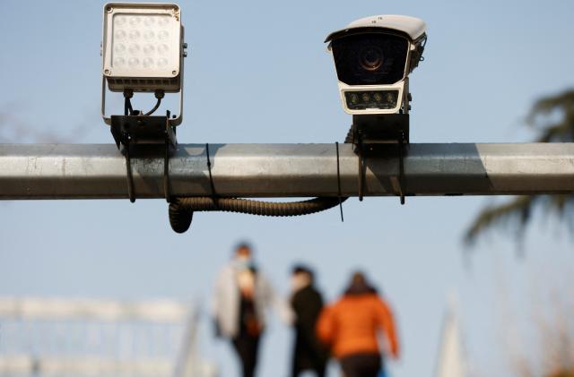 Pedestrians walk on an overpass near a surveillance camera overlooking a street in Beijing, China December 14, 2021. Picture taken December 14, 2021. REUTERS/Carlos Garcia Rawlins