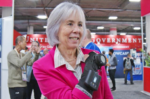 A person in a pink blazer wearing the GyroGlove hand stabilizer, holding their forearm and fist up to their chest. 