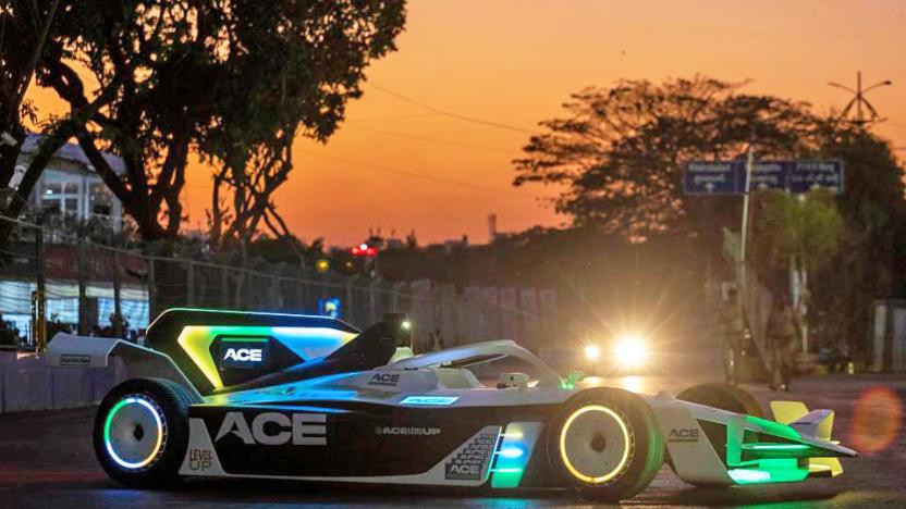 A modified Formula E Gen2 car with glowing accents in yellow, blue and green is seen on a street at dusk with the orange glow of the setting sun providing a warm setting.