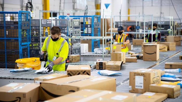An Amazon warehouse with workers boxing and taping with conveyor belts surrounding them.