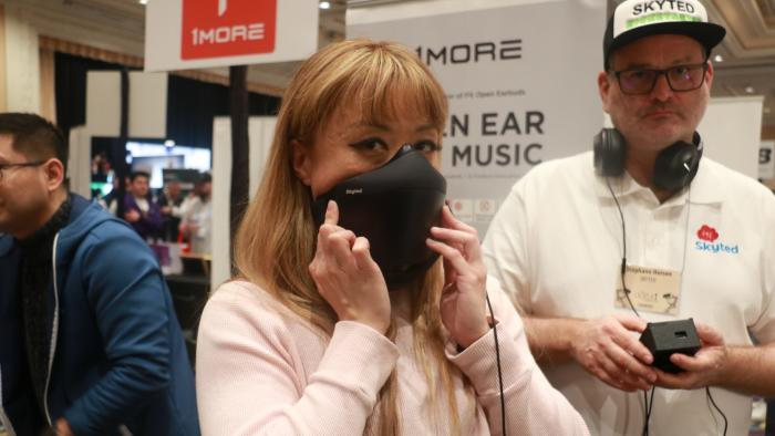 A person holding the Skyted mask to her face at a busy event with people and banners in the background.