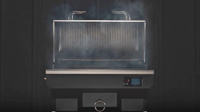 A head-on view of the Recteq SmokeStone 600 grill with its lid open and smoke wafting off the grill surface. Photographed in front of a black background.