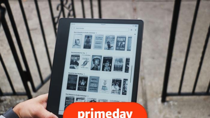 A person holds a Kindle Scribe ereader while sitting on the steps in a city. 