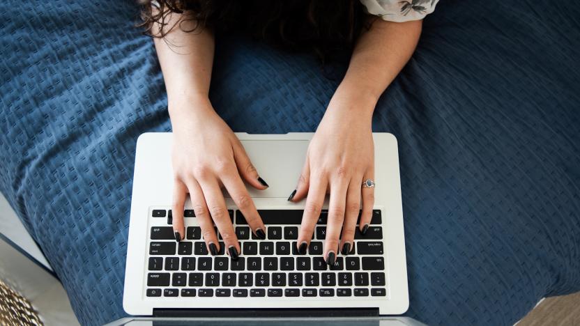 Detail of female hands typing on laptop on bed